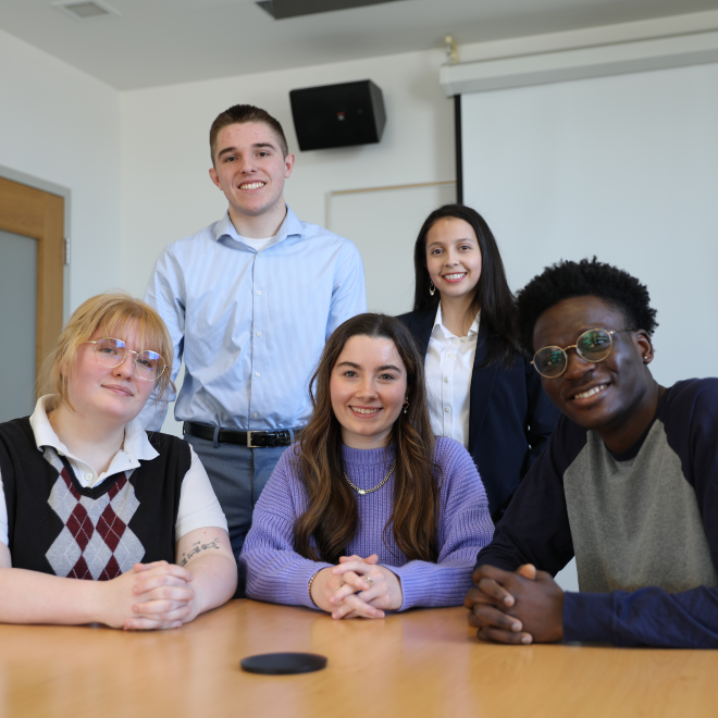 Five Forum on American Democracy scholars smile at the camera, gathered around a table—some seated and some standing—during a group photo.