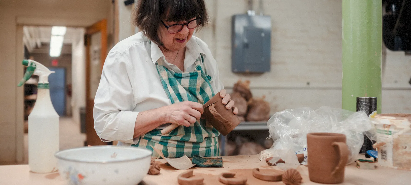 A woman working with clay to create mugs in the ceramics studio.
