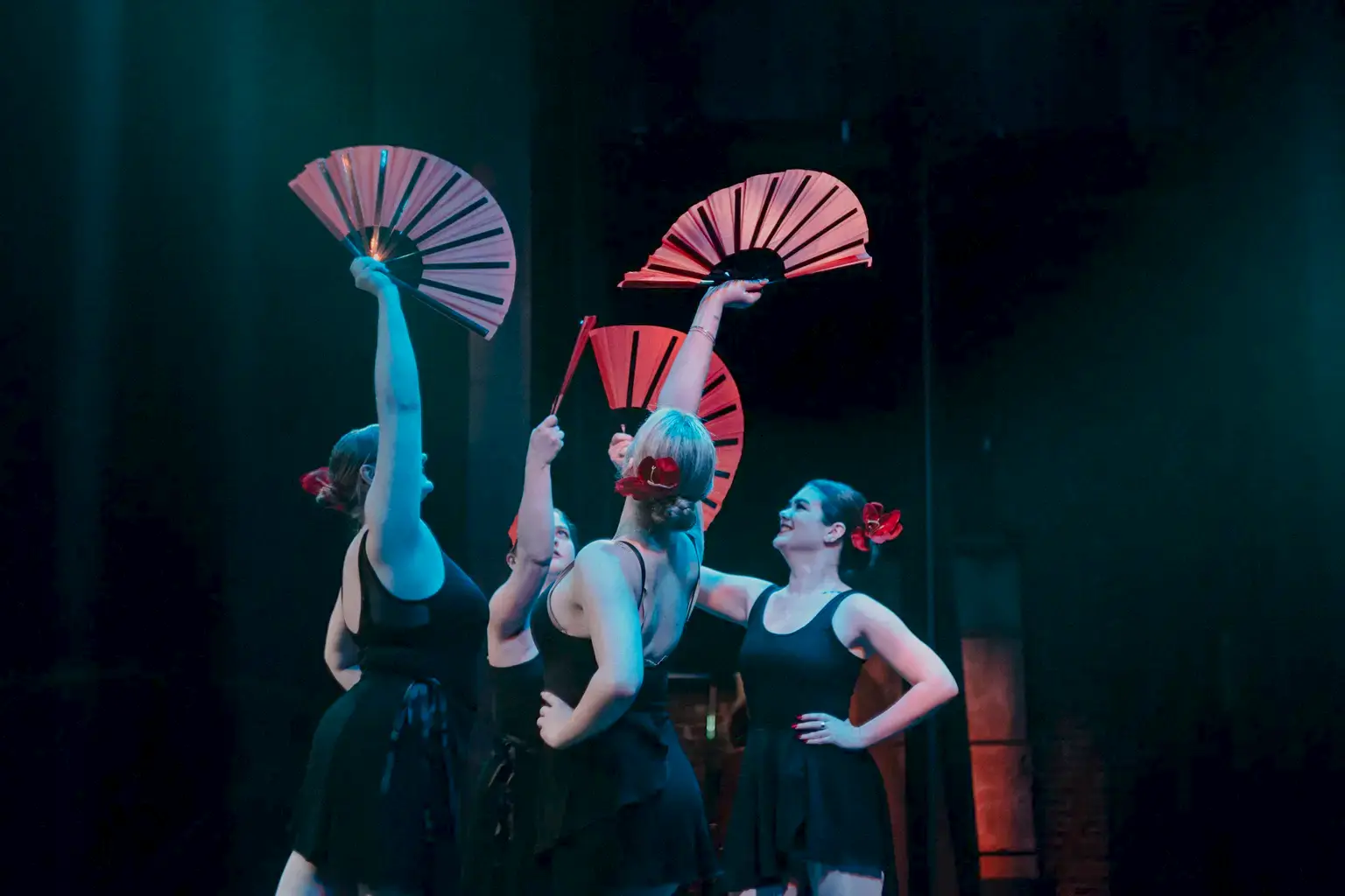 Four students with red and black folding hand fans perform on a stage.