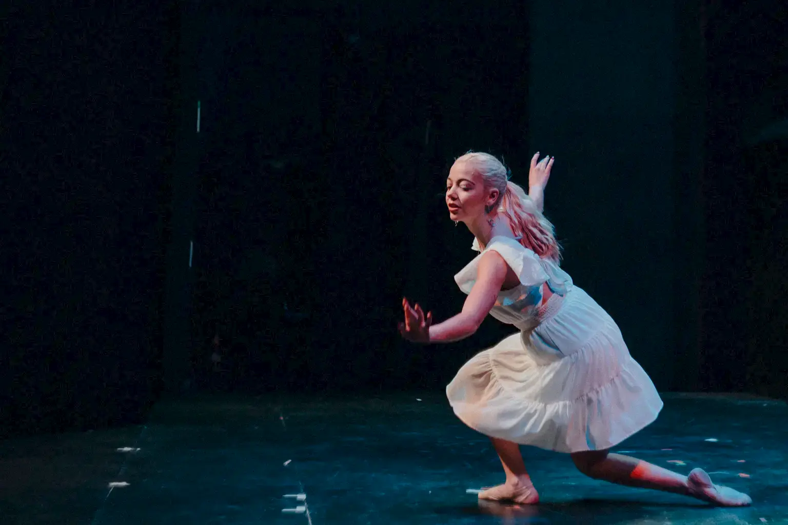 A student in a white dress dances on a darkened stage.