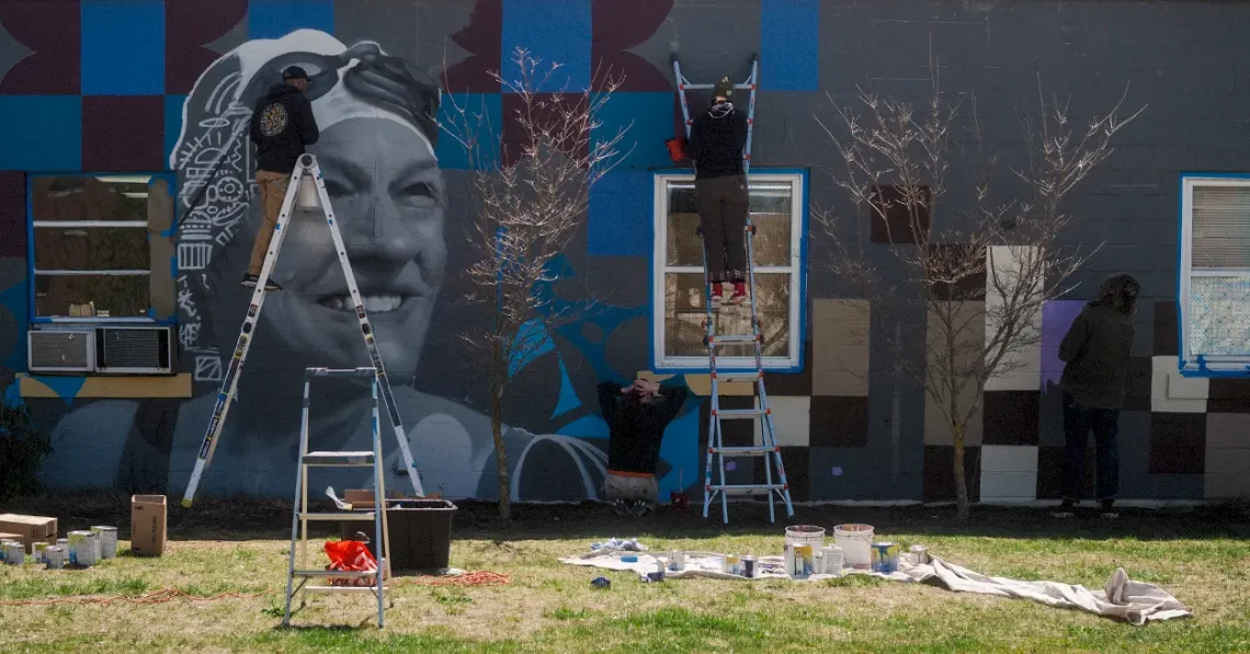 Ryan Adams and students painting a mural on an exterior wall.