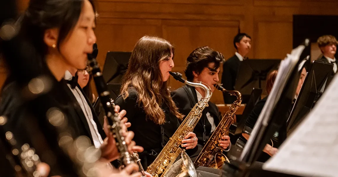 Young kids play clarinets and saxophones in an ensemble setting.