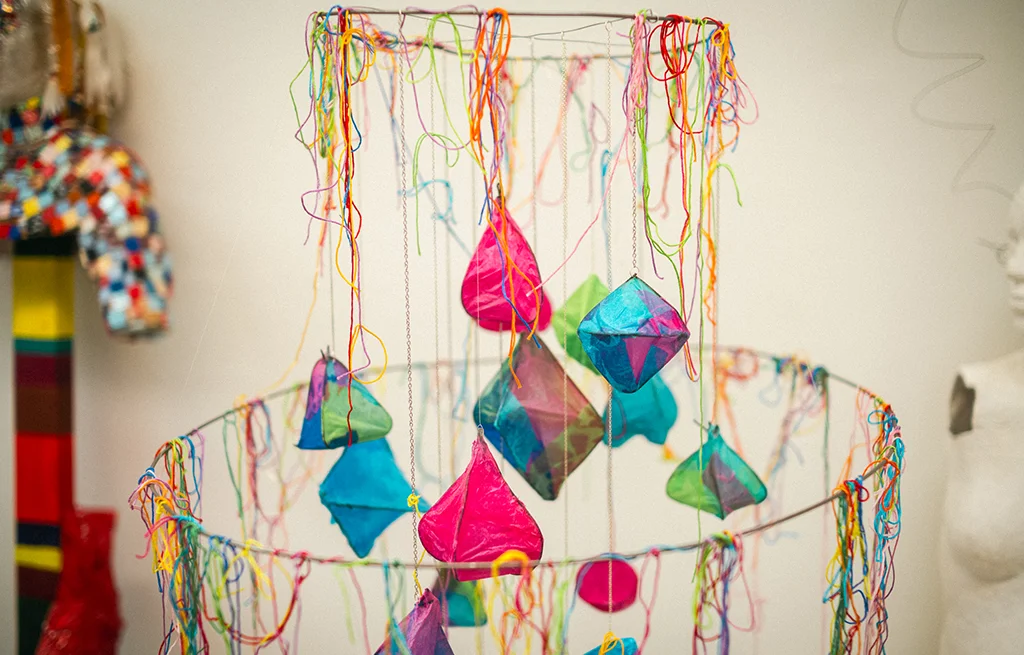 A tiered art piece featuring colorful string and paper ornaments.