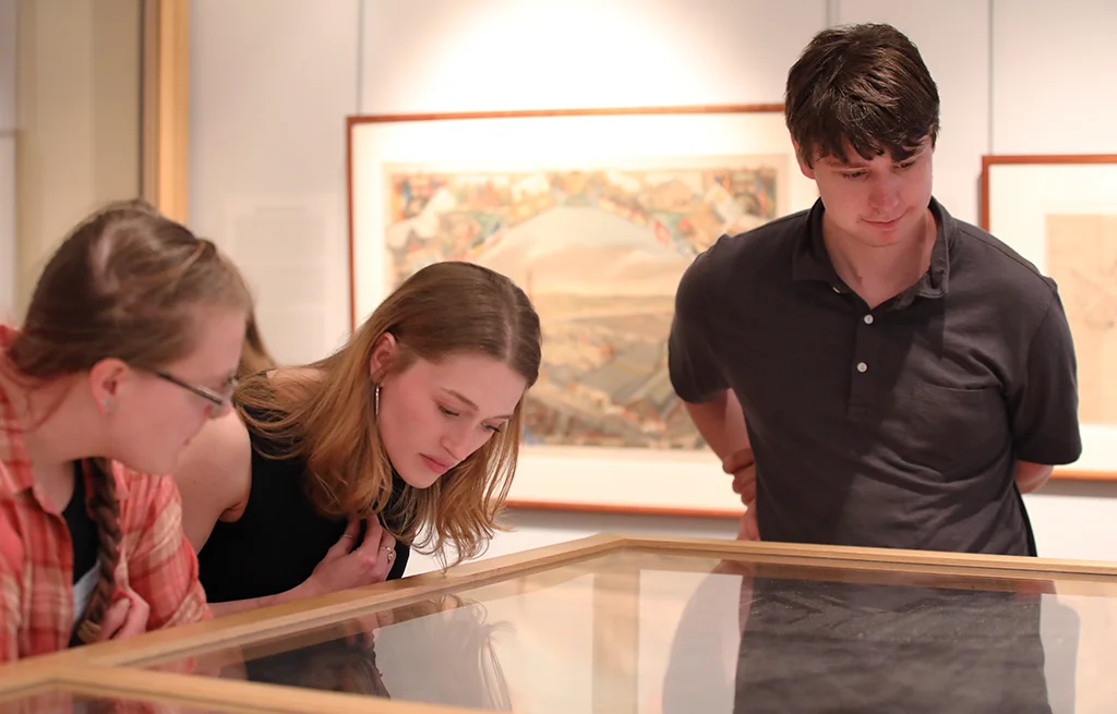 Three students examine maps within a glass case at the Osher Map Library.