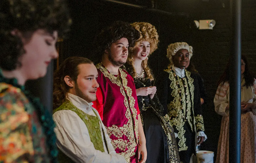 A group of theatre students in period costumes and wigs.
