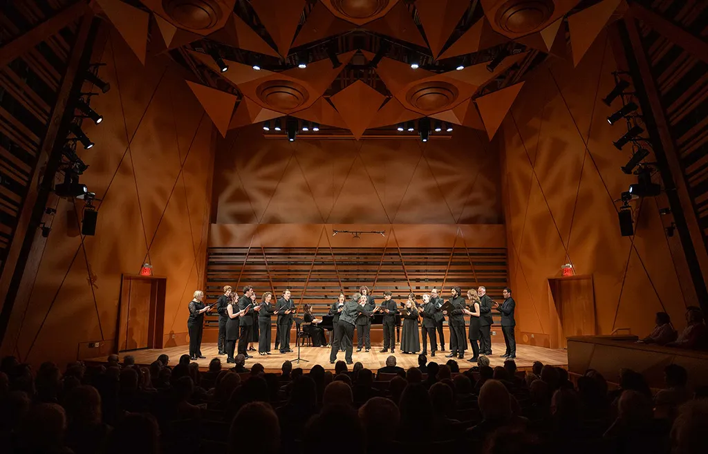 Several rows of audience seats face a brightly-lit stage with musicians dressed in all black.
