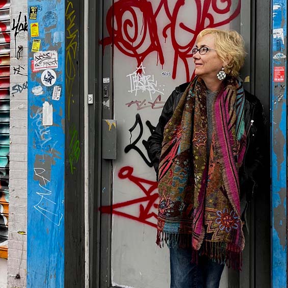 Photo by Judith Clute. Stonecoast faculty member and author Elizabeth Hand leans against a door frame of a building covered in stickers and graffiti.