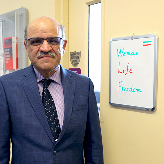 Professor Mehrdaad Ghorashi stands next to his office door where a small whiteboard has the words, "Woman, Life, Freedom" written in the colors the Iranian flag.