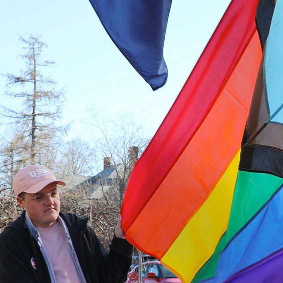 Kip Foster '23 holds up a corner of the Intersex-Inclusive Progress Pride Flag while it gets secured to a flagpole.