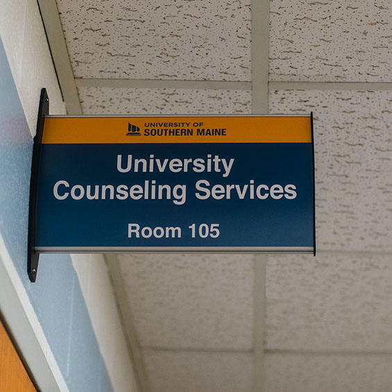 The University Counseling Services sign above room 105 in Payson Smith Hall. A drop ceiling is in the background.