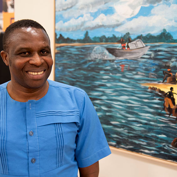 Rwandan artist Frederick Ndabaramiye stands next to one of his paintings in the Atrium Gallery on our Lewiston-Auburn campus.