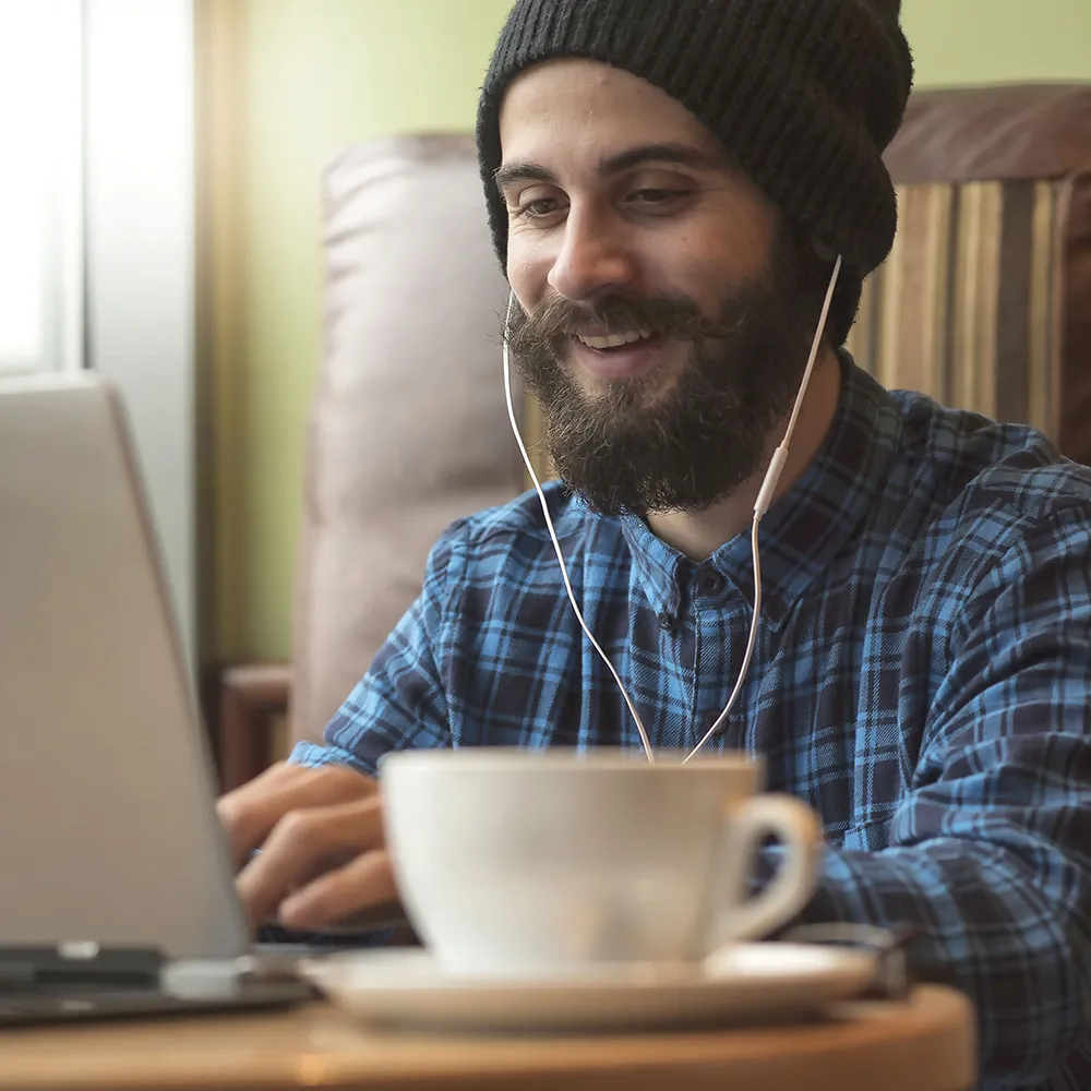 A student wearing headphones works on a laptop in a cafe.