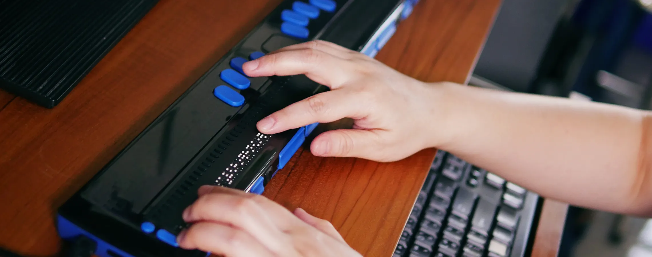 Two hands using a braille keyboard with blue buttons.