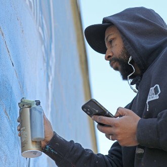 2024 artist-in-residence Ryan Adams applies spray paint to a mural in Westbrook.
