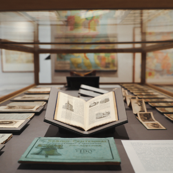 Close-up of archival books displayed in a glass case at the Osher Map Library gallery.