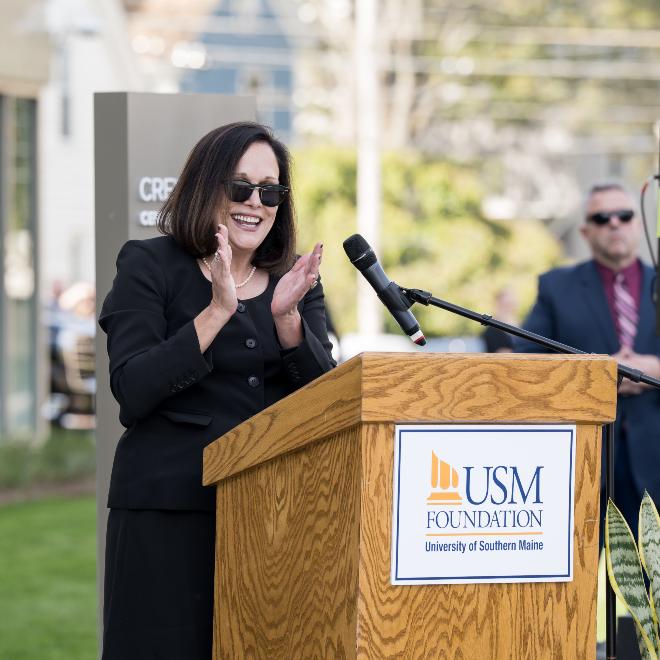 President Jacqueline Edmondson claps at a podium outside the Crewe Center for the Arts at the ribbon cutting ceremony.