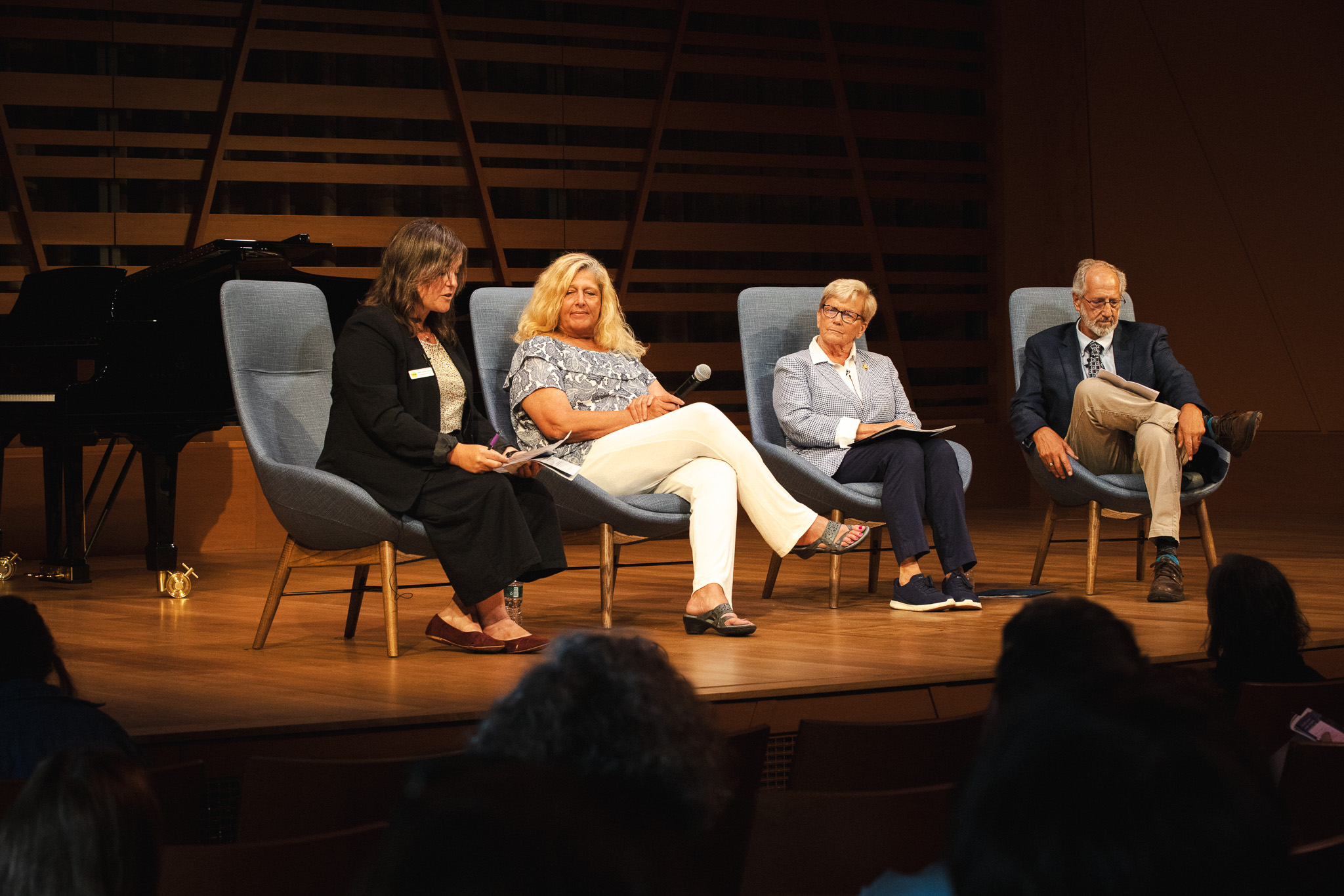 Mollie Cashwell speaks into a microphone during a panel discussion with NEA Chairman Mary Anne Carter, Congresswoman Chellie Pingree, and Maine Arts Commission Chair Bob Keyes, seated left to right, at USM's Crewe Center for the Arts.