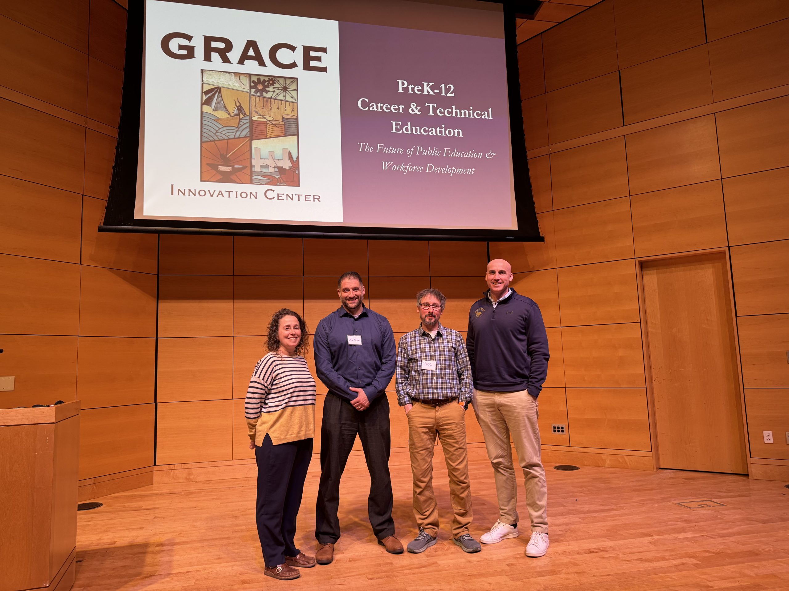 4 people standing on a stage with a projector screen behind them