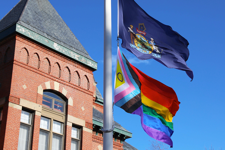 The Maine state flag and the Progress Pride flag fly over Corthell Hall on our Gorham campus.