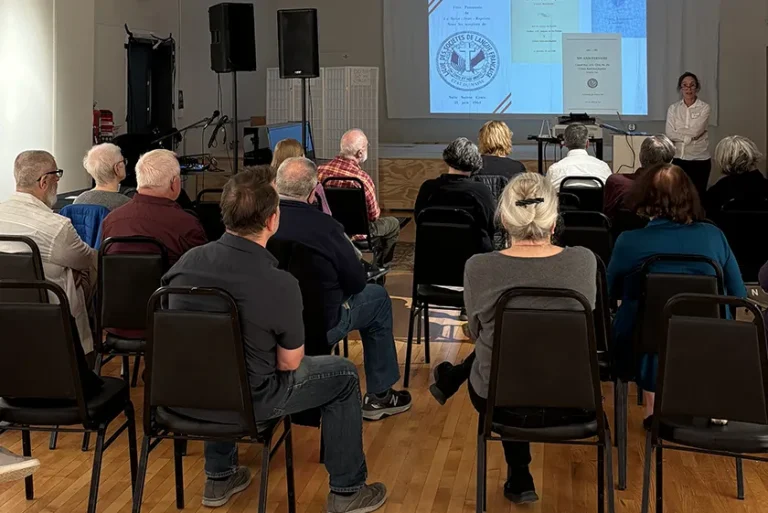 A group of people sitting in a large room facing a projected presentation.