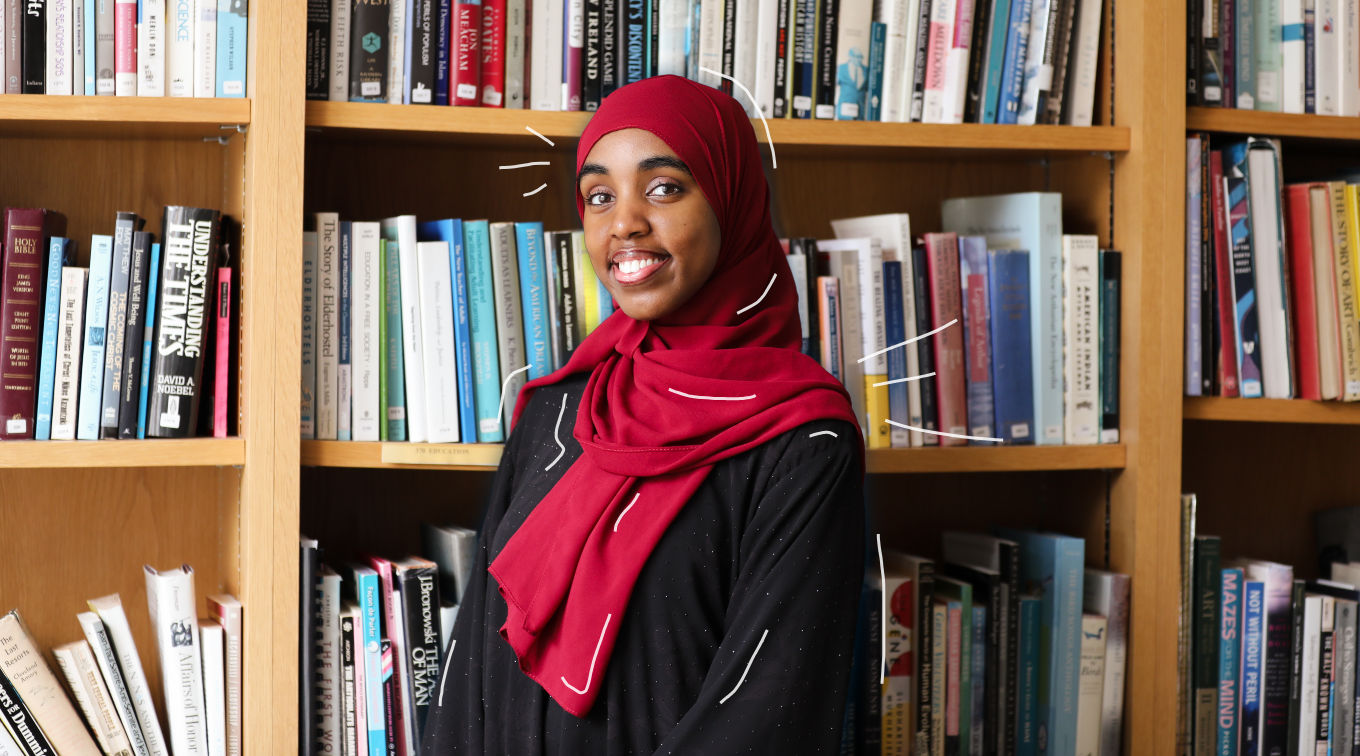 Najmo Ahmed smiles in front of a wall of bookshelves.