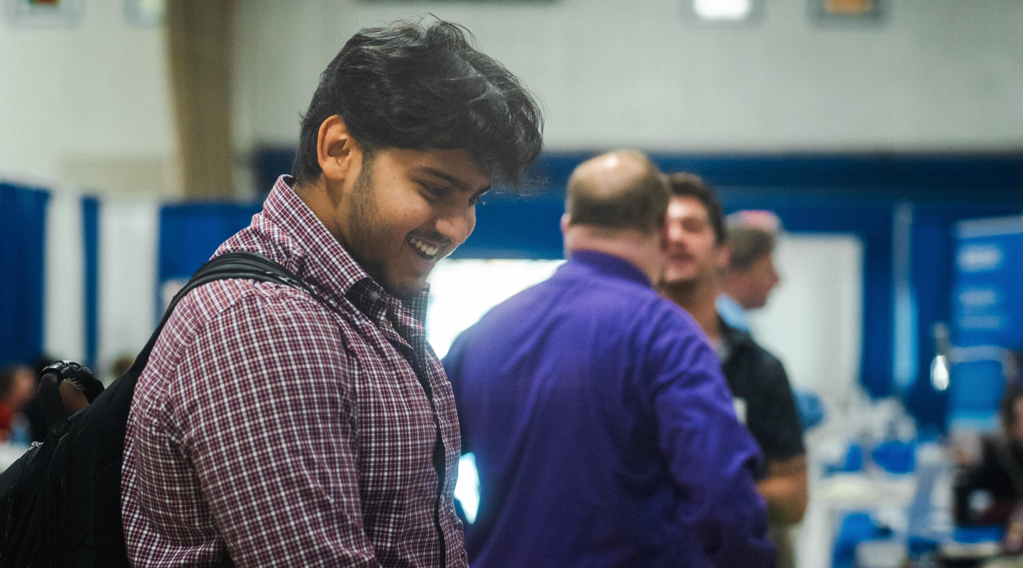 A student smiles while navigating a career fair, with a illustrated briefcase graphic overlaid on the image. A student smiles while navigating a career fair.