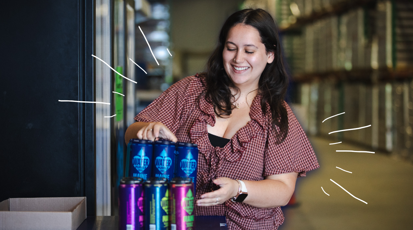 Olivia O'Donnell smiles while handling cans of mainelove water in the warehouse at mainelove's Westbrook facility.